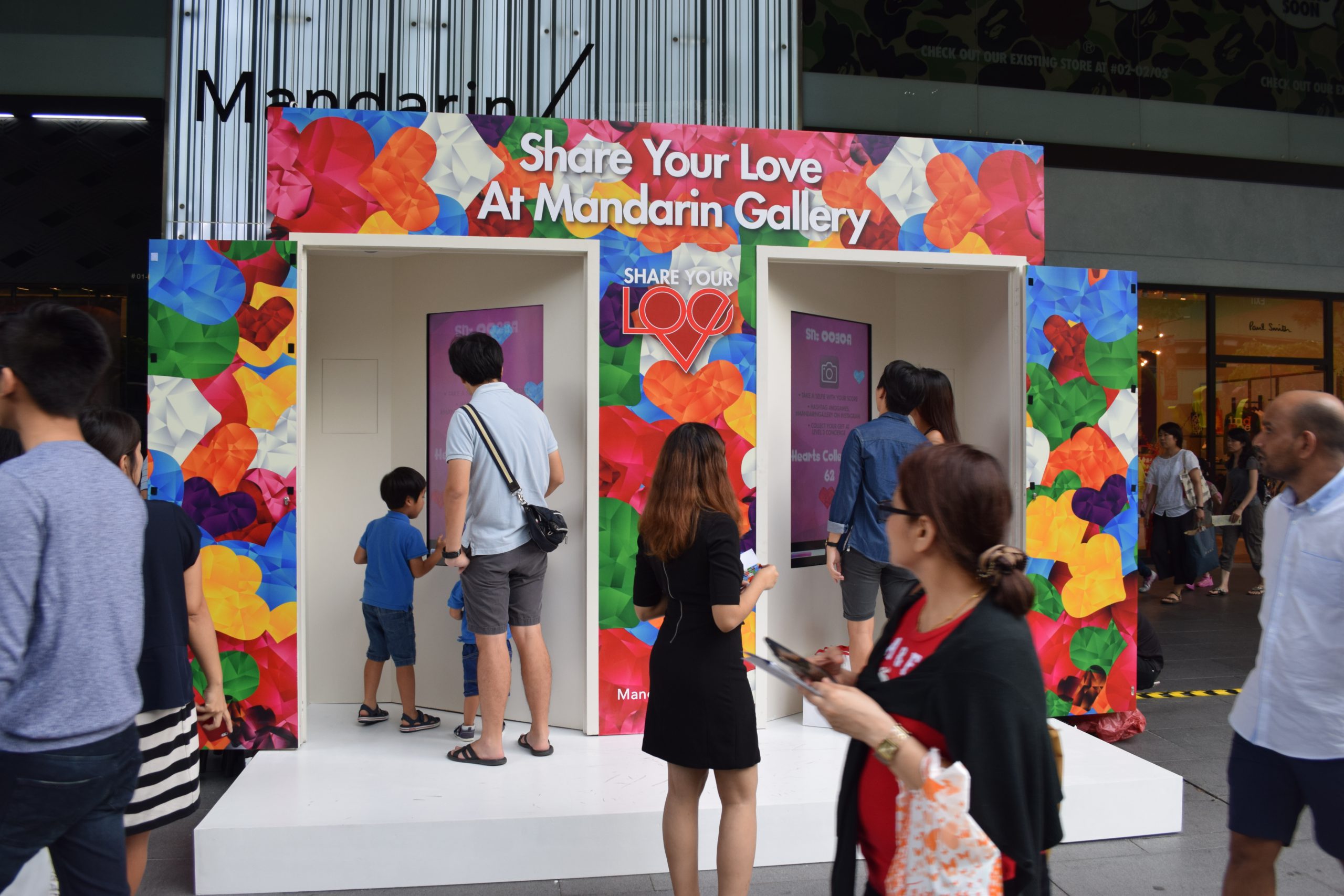 The curiosity of passers-by are piqued as they watch people play the Share Your Love social game outside of Mandarin Gallery