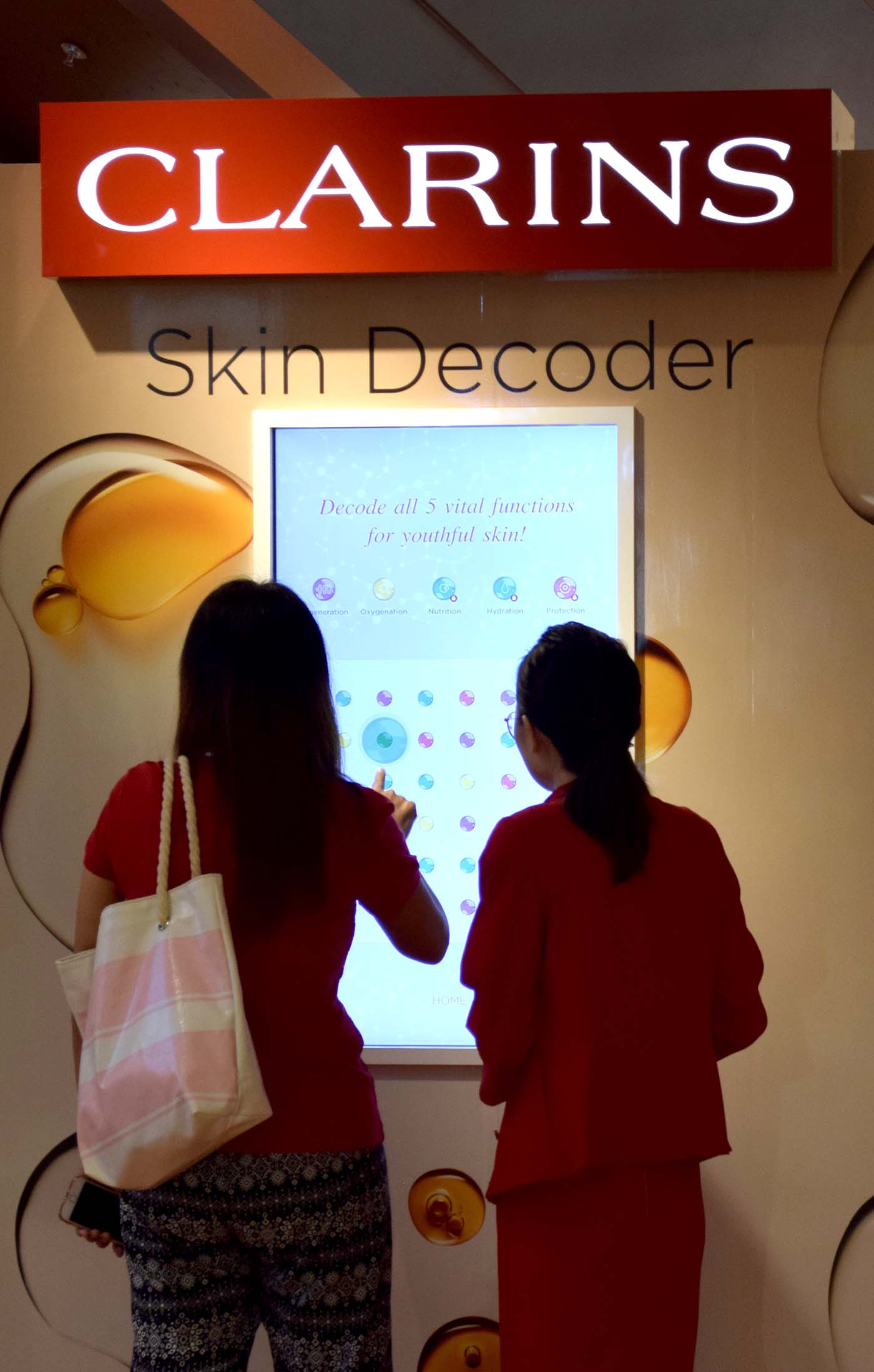 A lady plays the clarins digital game with the guidance of a helpful retail assistant